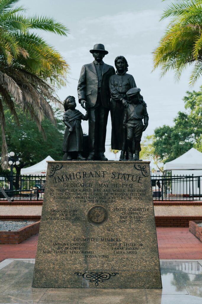 A monument honoring immigrants in Ybor City, Tampa, Florida under palm trees.