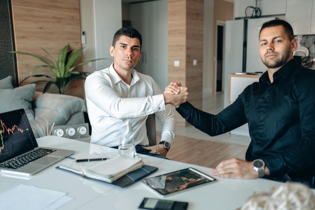 Two professionals agreeing on a deal while sitting at a desk in an office setting.